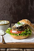 An aubergine burger with fried aubergine slices, Parmesan cheese, walnuts, tomato, lettuce and tzatziki