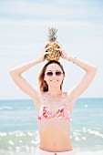 A young woman wearing a bikini holding a pineapple on her head