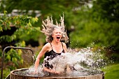 An older woman in a swimming costume jumping into a tub full of water in the garden