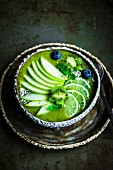 Grüne Smoothie Bowl mit Spinat, Banane, Apfel, Kokoswasser, Limetten, Kiwiblumen und Heidelbeeren