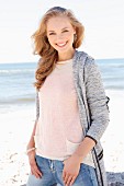 Dunkelblonde junge Frau in hellem Strickpulli, Strickjacke und Jeans am Strand