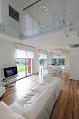 Eleganter, offener Wohnraum mit weisser Ledercouch und Edelholzparkett, Blick auf Glasbrüstung am oberen Etage