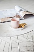 Mug and biscuit on saucer and magazine on white tray table