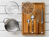 Kitchen utensils: a saucepan, a glass bowl, a measuring cup, cutlery and a whisk