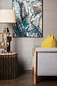 Grey armchair and table lamp below painting on wall