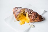 A croissant filled with salted egg yolk cut open on a baking parchment