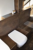 weiße Toilette in geflieste braune Sitzfläche integriert, Vormauerung mit Drückerplatte