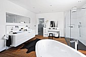 A bright white bathroom with a wooden floor, make-up table and shower area with glass panels