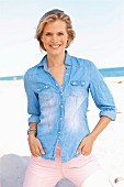 A young blonde woman on a beach wearing a light denim blouse