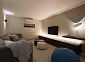 Elegantes Wohnzimmer mit langem Lowboard und indirekter Beleuchtung, seitlich moderne Tischleuchte auf Wandboard