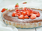 A chocolate tart topped with strawberries and icing sugar