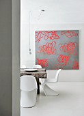 Einblick in minimalistischen Essbereich mit weissen Designklassikern, rustikalem Massivholztisch und moderner Kunst