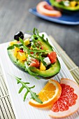 Avocado filled with a citrus fruit, mozzarella, olive and rocket salad
