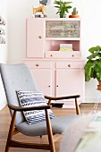 Patterned cushion on retro armchair in front of pink kitchen dresser