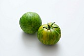 Zwei grüne gestreifte Tomaten vor weißem Hintergrund