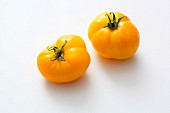Two yellow beefsteak tomatoes on a white surface