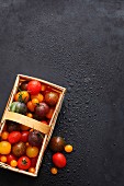 Various types of tomatoes in a wooden basket on a black surface
