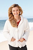 A young blonde woman on a beach wearing a red jumper and white teddy fleece jacket