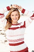 A young blonde woman on a beach wearing a striped knitted jumper