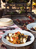 Black bean burritos and roasted chilli peppers on a wooden table outdoors