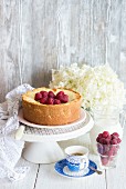 Vanilla cheesecake decorated with raspberries on a cake stand next to a cup of coffee