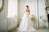 A young blonde woman wearing a wedding dress and looking out a window