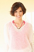 A brunette woman wearing a pink top and a transparent white knitted jumper