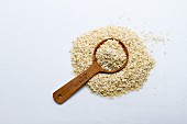 A pile of millet flakes with a wooden spoon on a white surface