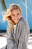 A young blonde woman in a white top and mottled grey knitted cardigan