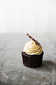 A chocolate cupcake with white chocolate cream on a marble surface.