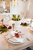 White place setting with silver cutlery and red cord around pine cone on festively decorated dining table