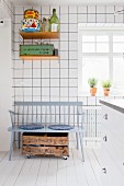 Weiß geflieste Küche mit grauer Holzbank, rollbarer Holzkiste und Wandboard mit Retro Blechdosen
