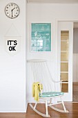 White rocking chair below framed picture and next to sliding door, motto on pennant and wall clock
