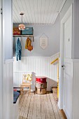 Wooden ceiling and foot of staircase in white, wood-clad, Scandinavian hallway with retro ambiance