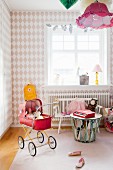 Diamond-patterned wallpaper and red retro dolls' pram in girl's bedroom