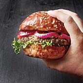 A hand holding a home-made beefburger with red onion
