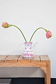 Two tulips in retro coffee pot on rustic wooden bench