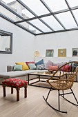 Rocking chair, upholstered stool and corner sofa with various scatter cushions in living area with glass ceiling