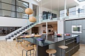 Black counter and gallery with glass balustrade in open-plan kitchen of loft apartment