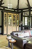 Industrial-style leather couch and side tables in front of glass-fronted bookcase in half-timbered house