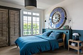 Petrol-blue dado, matching bed linen and round artwork on wall in bedroom