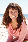 A brunette woman in a pink long-sleeved top on the beach
