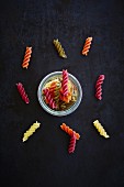 Colourful fusilli in a glass and scattered next to the glass