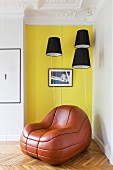 Lounge-Ledersessel vor gelber Wand und schwarzen Lampenschirmen in restaurierter Altbauwohnung