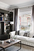Scatter cushions on white sofa and coffee table in front of window and shelving