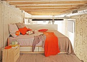 Sleeping area with orange accents below exposed beams and ventilation ducts in loft apartment