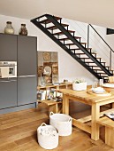 Solid wooden furniture in dining area of open-plan kitchen next to steel staircase