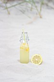 A bottle of lemonade with a lemon in the sand