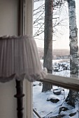 Lamp in front of window with view of trees in snowy landscape through window