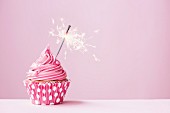 Cupcake mit Wunderkerze vor rosa Hintergrund